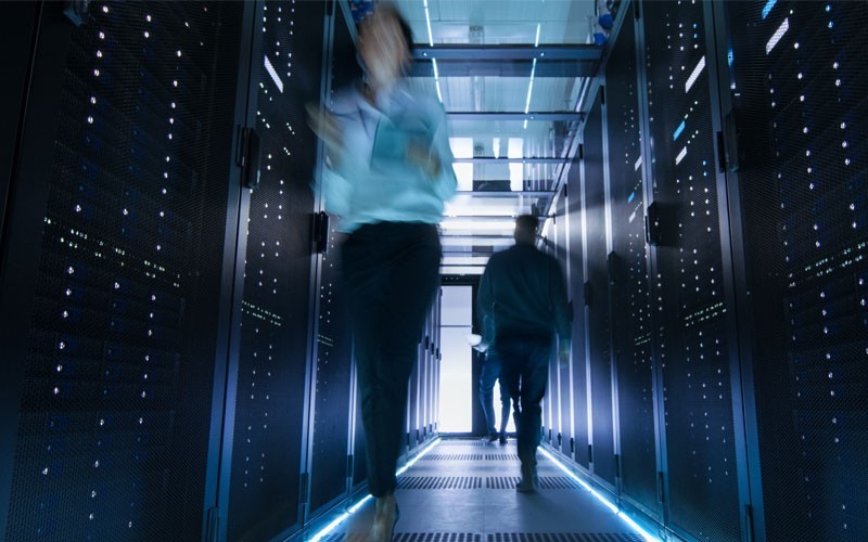 Accelerate your time to market and reduce your infrastructure maintenance costs Two people walking through data centre
